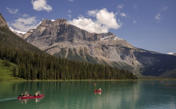 Canoes on Emerald Lake surrounded by forest and the Canadian Rocky Mountains under a clear sky