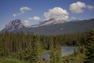 A tranquil mountain landscape of the Canadian Rocky Mountains with a lake, forest, and fluffy