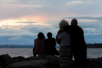 Silhouetted family watching a colorful sunset by the water in Ottawa, Ontario, Canada, North