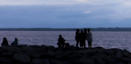 Group of silhouetted figures by a municipal lake at dusk in Ottawa, Ontario, Canada, North America