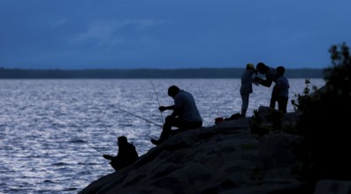 Silhouetted figures fishing and interacting by a lake at night in Ottawa, Ontario, Canada, North