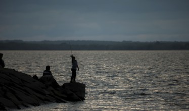 A person fishing on a rocky shore at dusk with a calm lake in Ottawa, Ontario, Canada, North