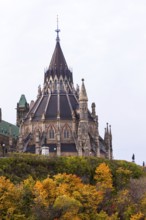 A Gothic-style Canadian Parliament building with a prominent spire, surrounded by colorful autumn