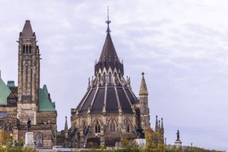 The Canadian Parliament Buildings with an ornate spire and towers against a cloudy sky, showcasing