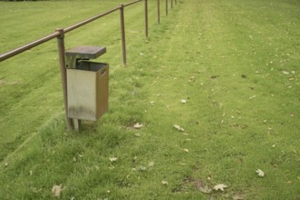 Borken, NRW, Germany, Empty metal garbage bin standing next to a railing in a public park with