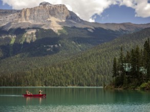 Canoe on Emerald Lake encircled by the Canadian Rocky Mountains and dense forest under a bright sky