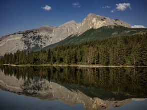 Mountainous landscape of the Canadian Rocky Mountains with dense forest reflected in a calm lake