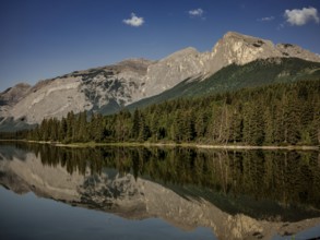 Quiet, reflective waters mirror the surrounding Canadian Rocky Mountains and forest near Canmore,