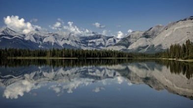 Majestic mountains of the Canadian Rocky Mountains and forest reflected in calm lake under a clear