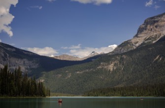 Canoe on a serene Emerald Lake surrounded by the Canadian Rocky Mountains under a blue sky with