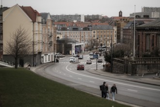 City street view with cars and pedestrians, lined with historic buildings under a gray sky in