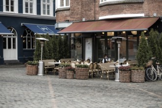An empty outdoor cafe with wicker chairs and planters on a cobblestone pavement in Aarhus, Denmark,