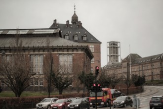Cars stopped at a red light near historical brick buildings and bare trees on a cloudy day in