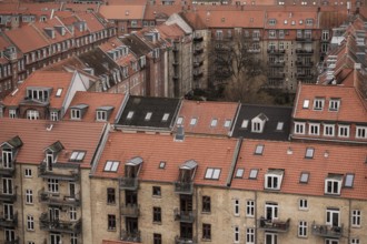 Rooftop view of densely packed residential buildings with red tile roofs under an overcast sky in