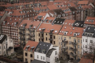 View of a residential area with red-tiled rooftops and brick buildings under a cloudy sky in
