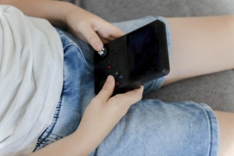 Child hands holding and playing portable video game console during leisure time