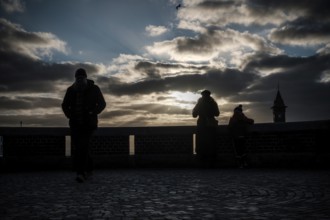 Silhouetted figures at sunset with dramatic clouds and a distant tower in Helsingborg, Sweden,