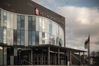 Helsingborg Arena featuring a glass facade, flags, and situated under cloudy weather in