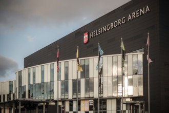 Modern architecture of Helsingborg Arena with flags and large windows under an overcast sky in