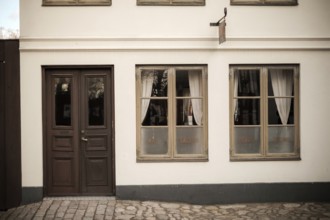 A vintage building facade with wooden doors and windows, featuring cobblestone pavement in