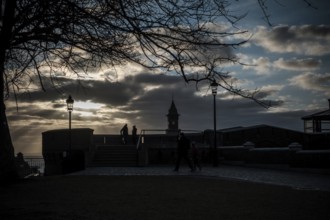 Figures silhouetted against sunset with dramatic clouds, tree, and lampposts in Helsingborg,