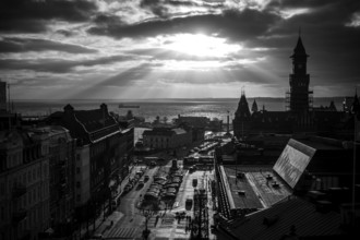 Black and white cityscape with dramatic clouds and sunlight over a harbor and buildings and looking