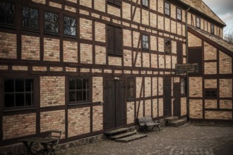 Historic brick building with wooden beams and benches, featuring cobblestone pavement in