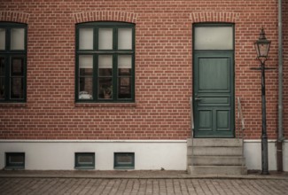 Brick building with a green door and windows, featuring a vintage lamppost on the sidewalk in
