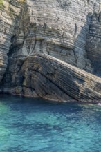 Sunny illuminated detail of the ligurian coast showing a layered rock formation and blue sea