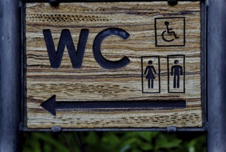 Wooden sign indicating direction of public toilet facilities for all users in ronda, malaga, spain