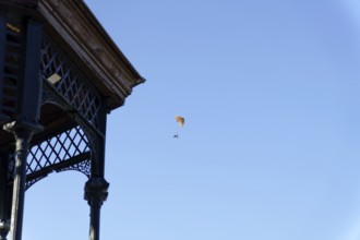 Paramotorist flying with a powered parachute against a bright clear blue sky, next to an old gazebo