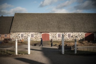 Stone building with red doors on a farm, people walking dogs in foreground in Helsingborg, Sweden,