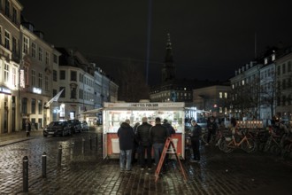 Night scene with people gathered around a food stand on a cobblestone street in Copenhagen, Denmark
