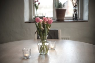 Close-up of a vase filled with tulips on a wooden table, with soft candle lights in Helsingborg,