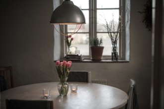 A cozy dining area with a round table, tulips in a vase, and soft lighting from a pendant lamp in