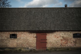 A rustic brick building with a red door under an overcast sky, featuring a chimney in Helsingborg,