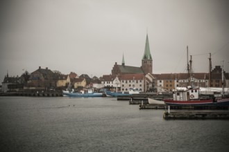 A harbor with docked boats and a church in the background on a cloudy day in Helsingor, Denmark,