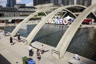 Public plaza in Toronto with arches over a fountain and people enjoying the sunny day in Toronto,