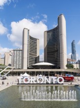 Toronto sign by a fountain against a backdrop of Toronto City Hall at Nathan Phillips Square in
