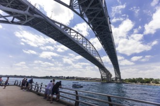 Viewers on a riverside pier looking at the expanse of the Blue Water Bridge connecting Canada and