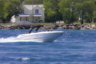 A speedboat glides quickly across the water with trees and houses in the background along the St.