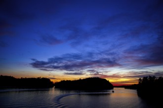Boat sails on a serene lake during sunset, creating a vivid twilight sky in Muskoka, Ontario,