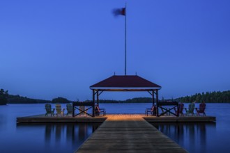 A tranquil lakeside dock with chairs and a flag at dusk in Muskoka, Ontario, Canada, North America