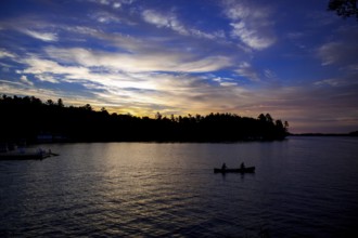Silhouettes of two canoes on a lake at sunset, creating a peaceful landscape in Muskoka, Ontario,