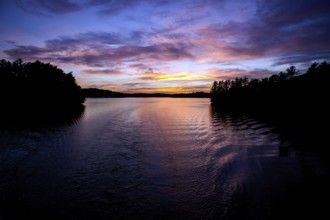 Calm water reflects a colorful evening sky, creating a peaceful twilight landscape in Muskoka,
