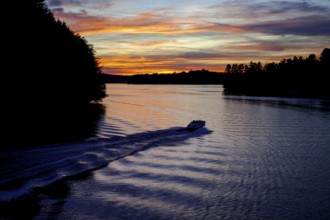 A boat moves across a lake during twilight, leaving ripples under a colorful sunset in Muskoka,