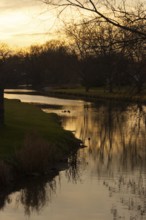 Tranquil scene of a creek at sunset with silhouetted trees and warm reflections in the water in St.
