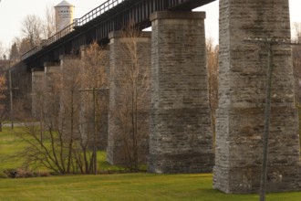 Image of a stone bridge structure with green grass and trees, highlighted by warm tones in St.