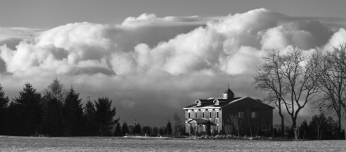 Monochrome image featuring a house against a backdrop of billowing clouds, evoking a serene winter