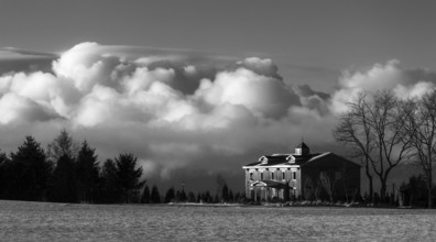 Black and white image of a house with dramatic clouds in the background, creating a moody winter